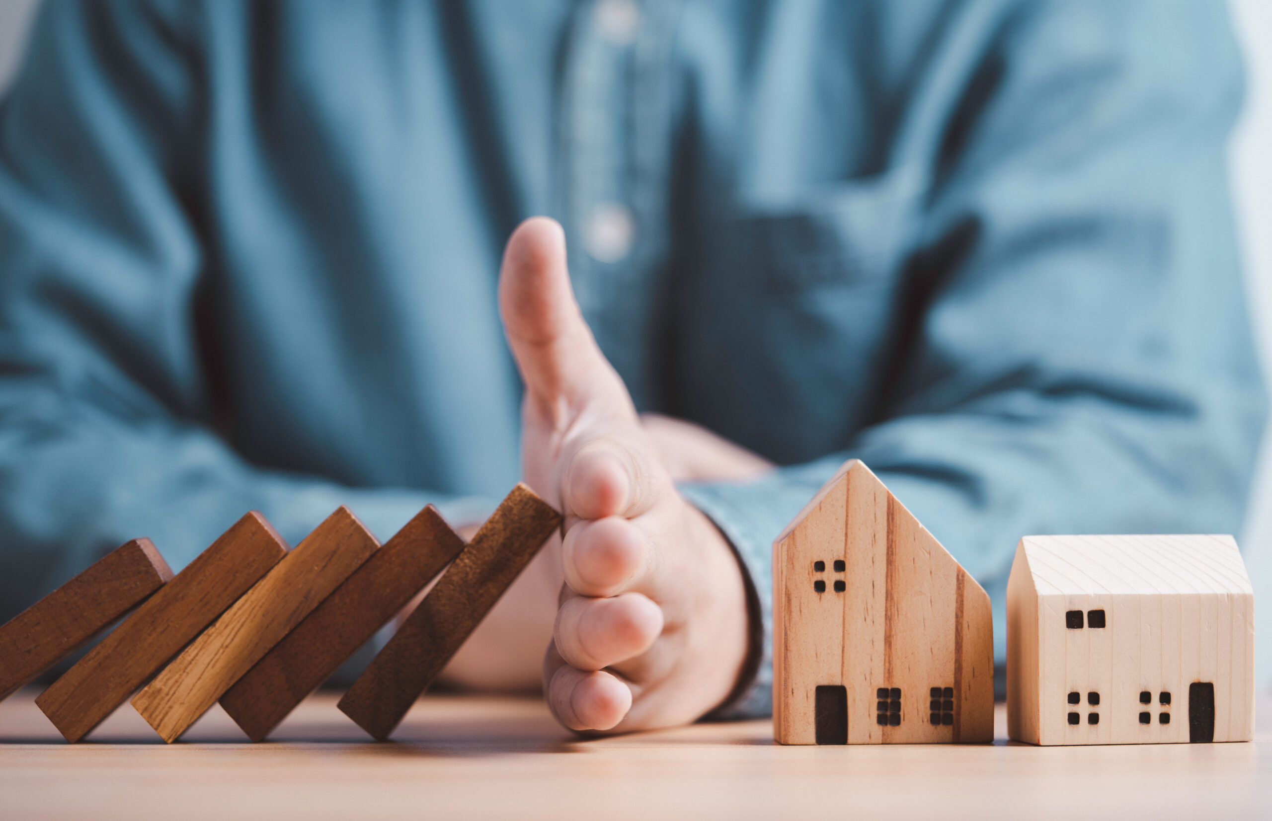 Hand protecting houses from domino falling to exemplify an article about Avoid These 10 Mistakes When Investing in Real Estate - Real Estate Juan Cano, Massachusetts